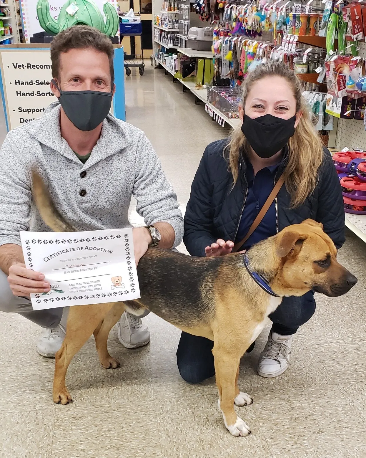 Marty standing in a pet store aisle between two kneeling people in face masks, one holding a certificate of adoption